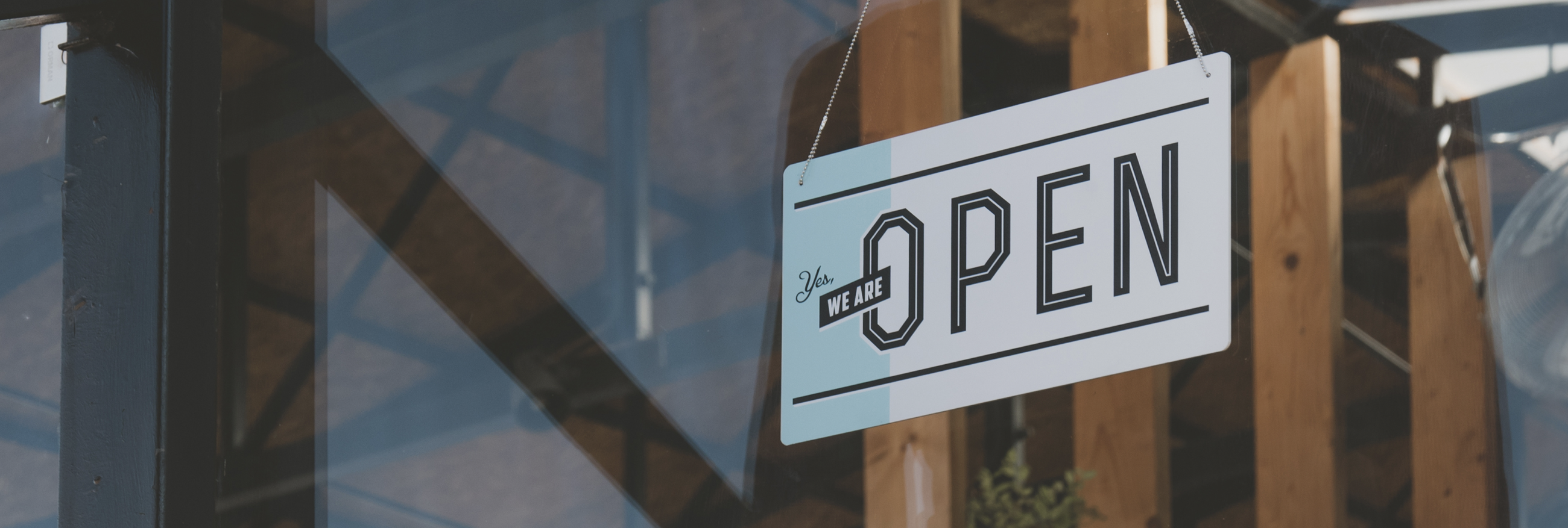 A photo of a we are open sign hanging on the entrance door of a small cafe.