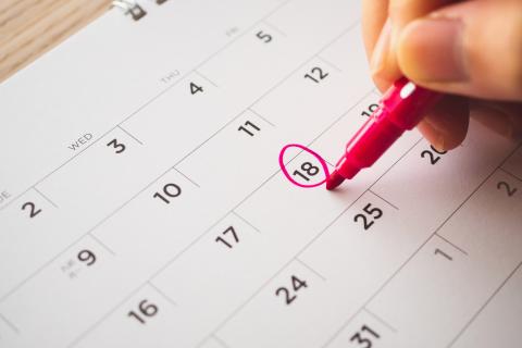 Hand with pen mark on calendar date.