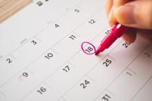 Hand with pen mark on calendar date. 
