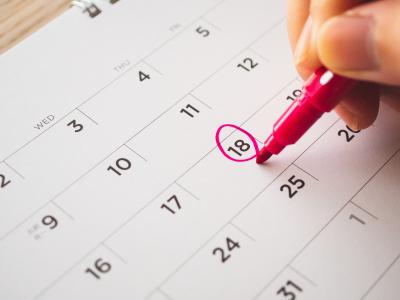 Hand with pen mark on calendar date. 